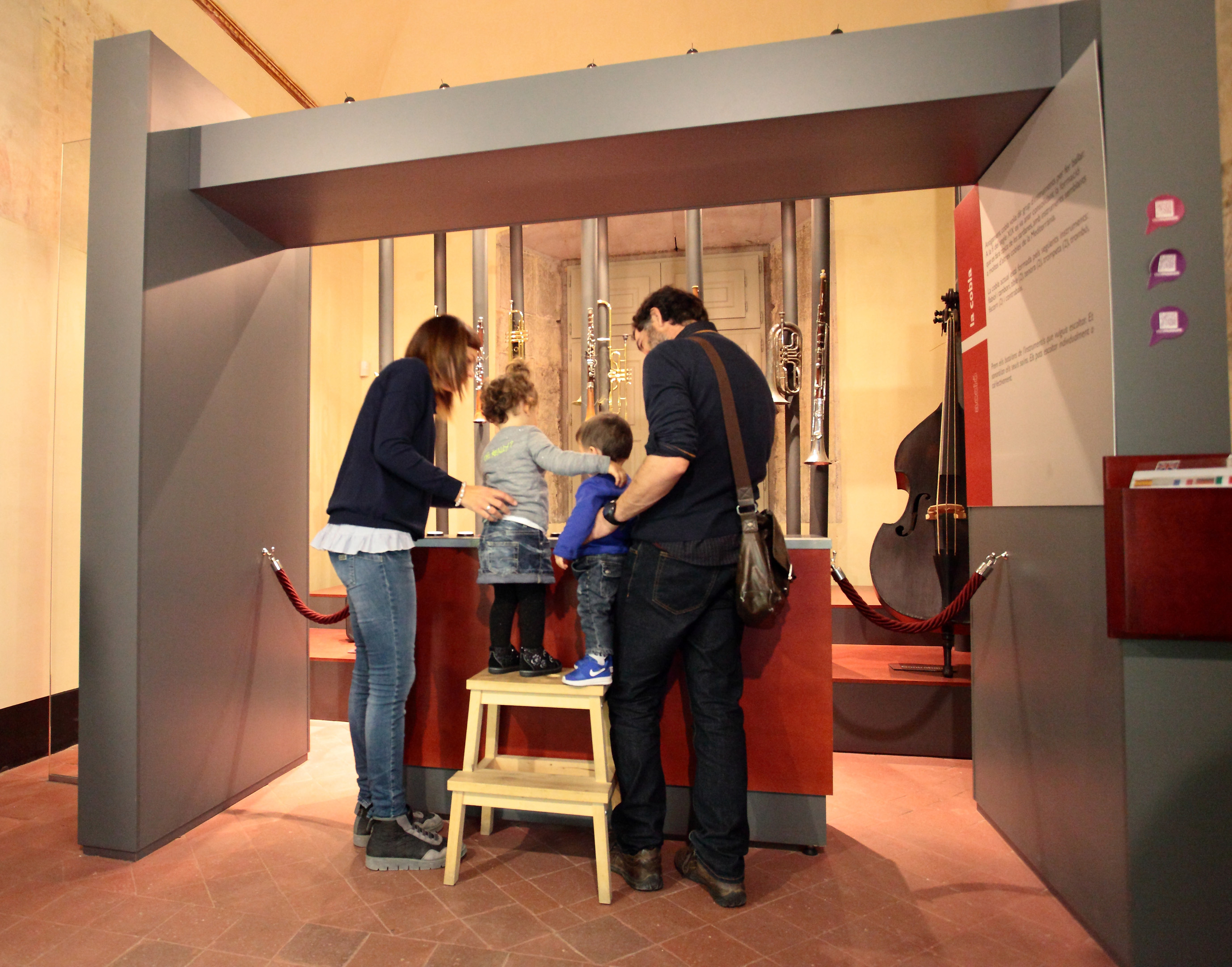 pares amb dos nens enfilats a un taburet per tocar uns instruments a una sala del Museu de la Mediterrània 