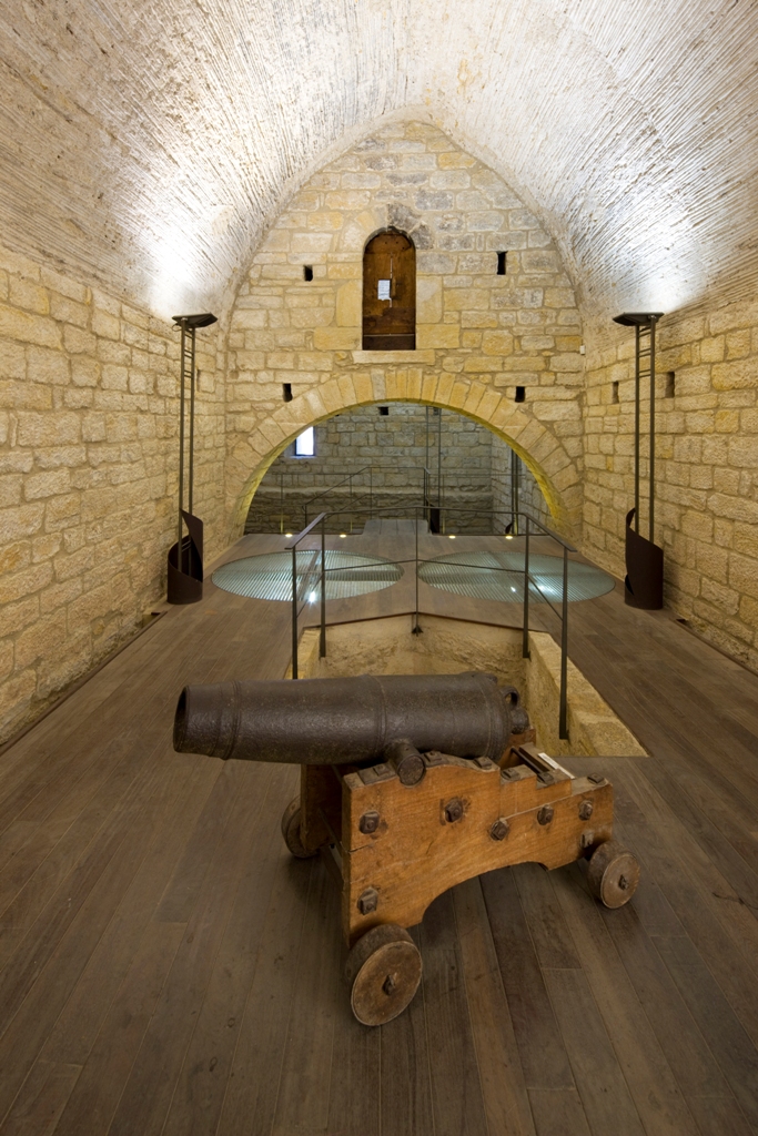 Interior del castell - palau de la bisbal. Un canó a primer terme i un arc de mig punt al fons de la sala