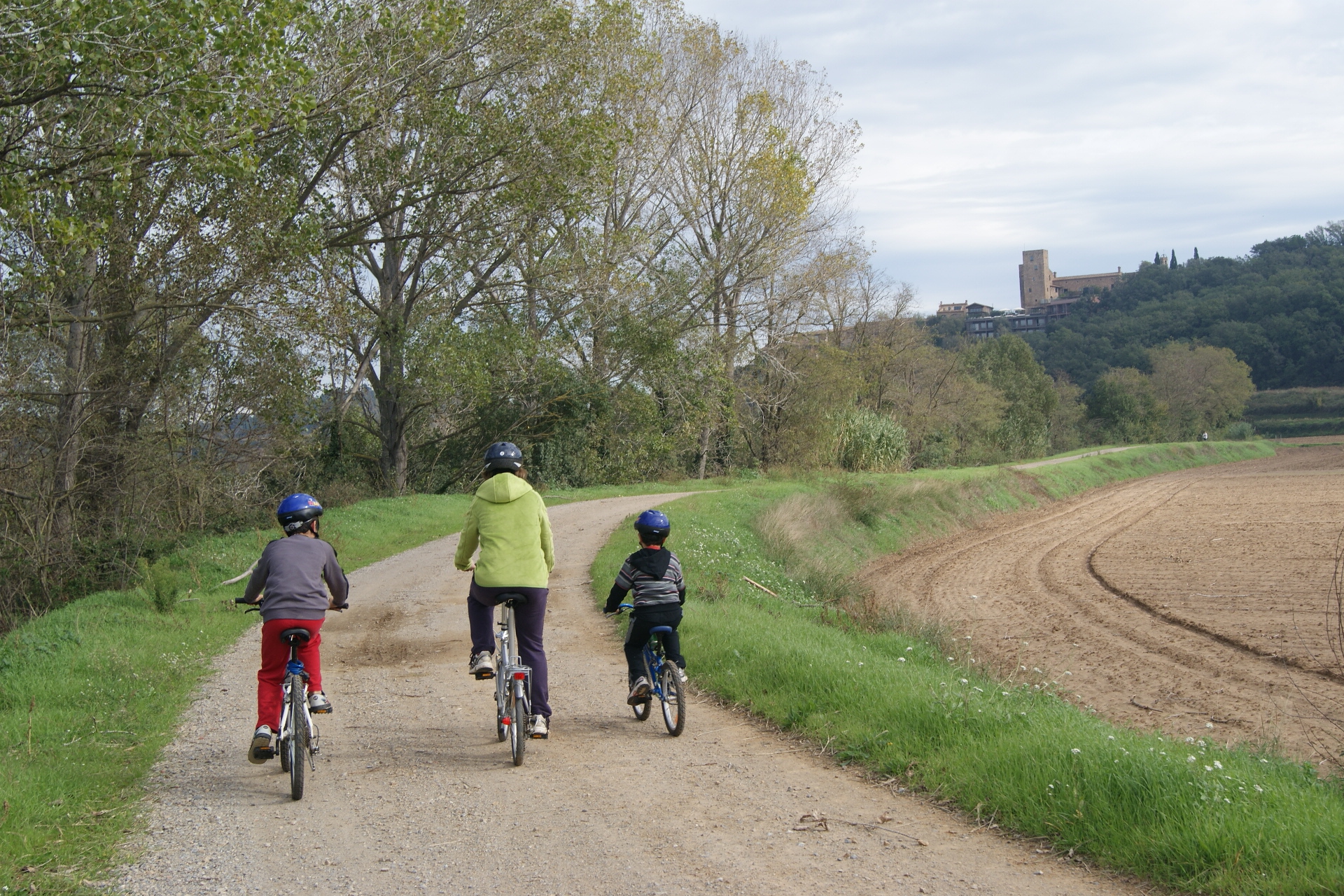 mare amb dos fills amb bicicleta que van per un camí de sorra que els porten al castell d'empordà