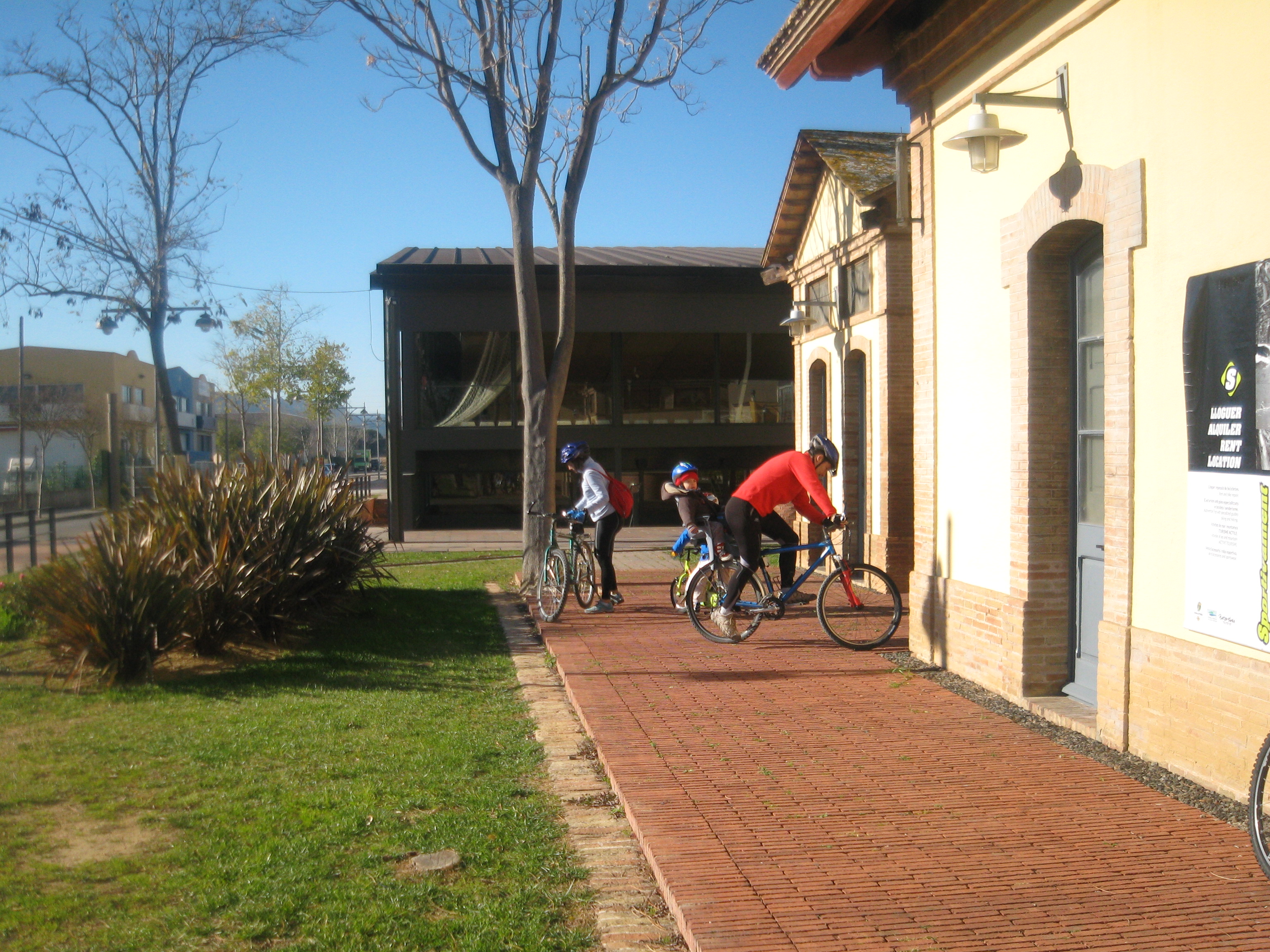 antiga estació del carrilet castell d'aro a mà dreta. una parella mb bicicleta amb el seu fill petit a darrere el seient