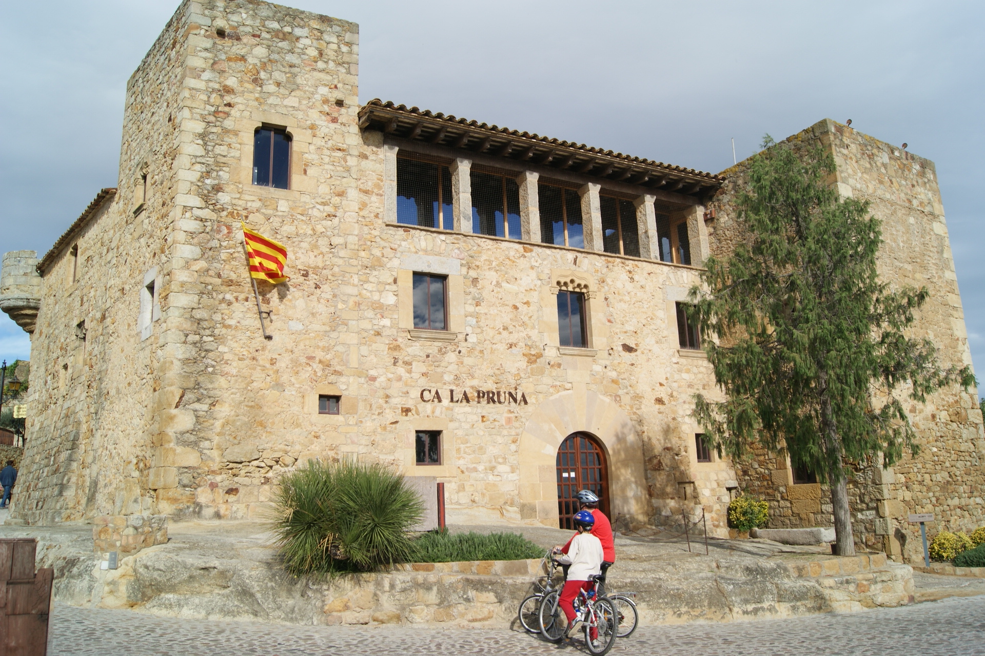 casa fortificada Ca la Pruna de Pals i amb una parella amb bicicleta a davant