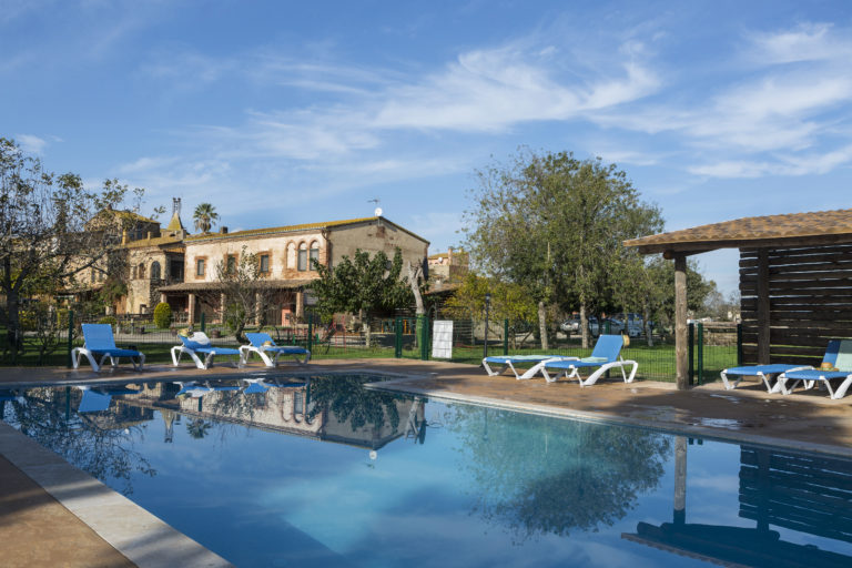 Piscina a primer pla i a darrera la casa rural Can Pujol. Masia 