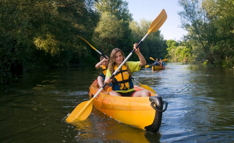 A primer pla kayak pel riu ter amb un noi i una noia, semblen joves. i a darrera un altre kayak amb una parella, semblen els pares