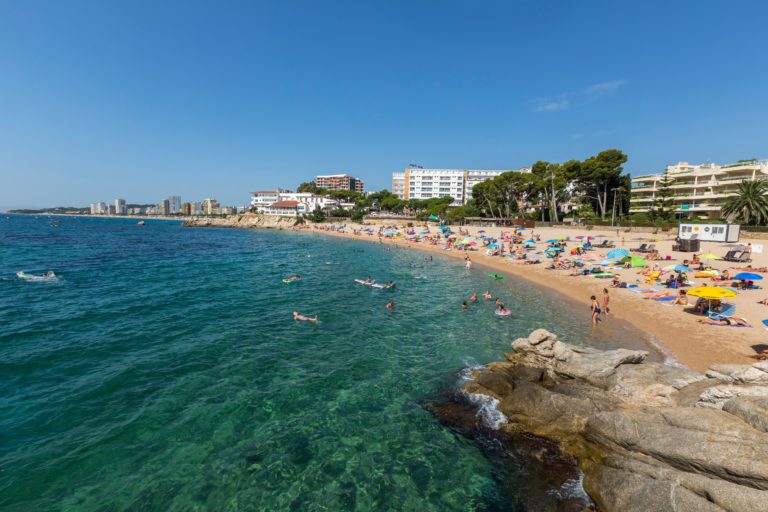 platja de sant antoni, mar a l'esquerra i platja amb persones prenent el sol i amb parasols a la sorra