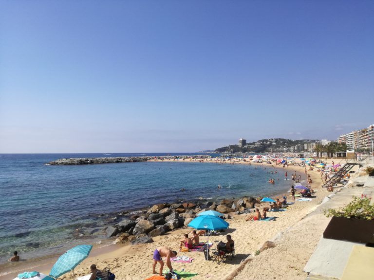 platja de sant antoni, mar a l'esquerra i platja amb persones prenent el sol i amb parasols a la sorra