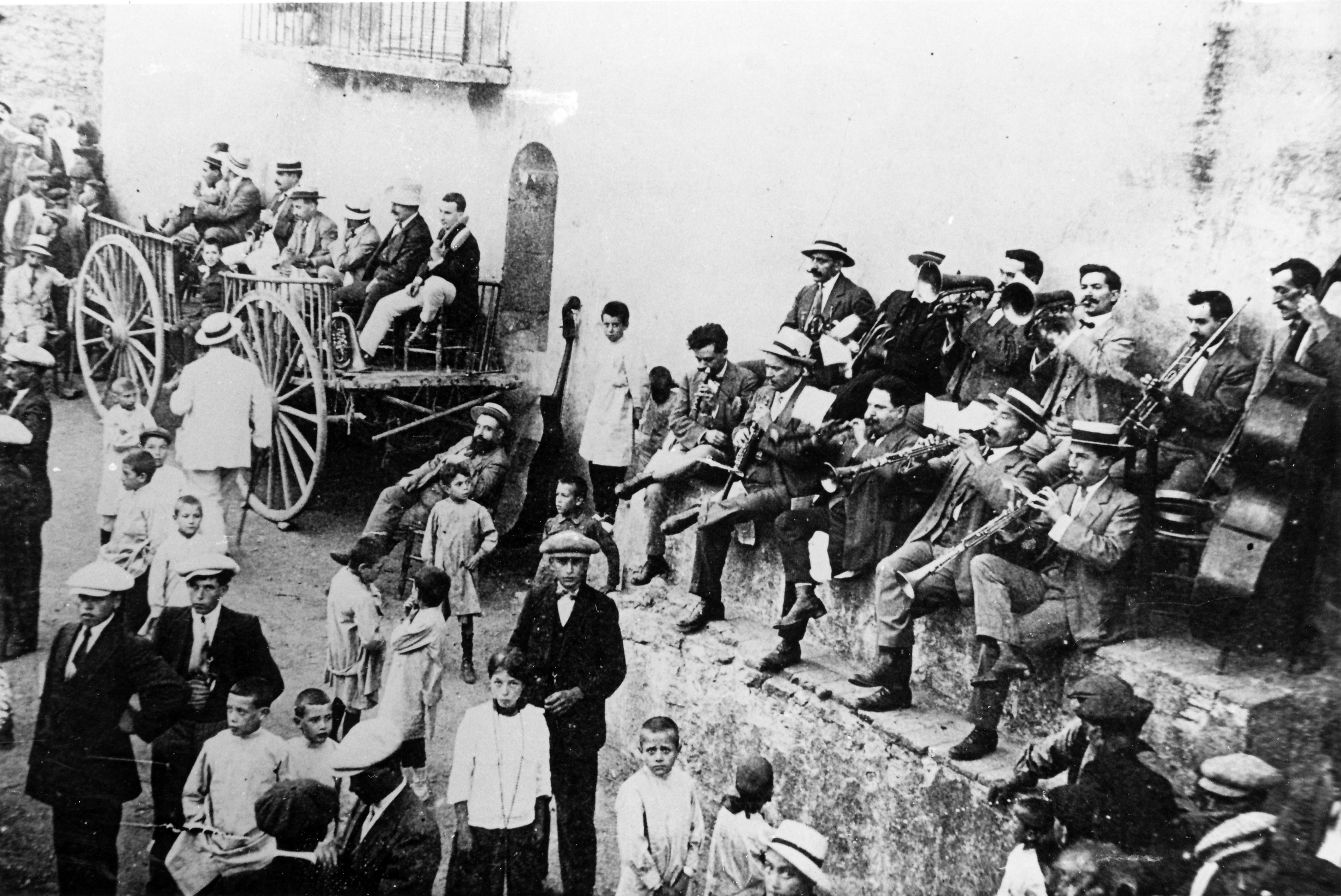 En una plaça de poble, un grup de músics en format de cobla toquen. És una fotografia antiga dels anys 50. 