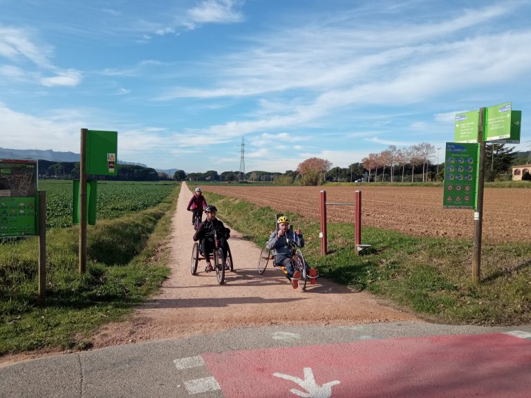 dos homes en hanbike en primer pla i una dona amb bicileta al fons