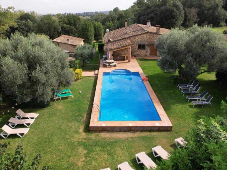 Piscina a primer pla i a darrera la casa rural Can Pujol. Masia