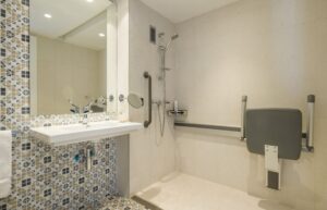 socorrista que acompanya a una nena amb una cadira que no és del tot amfíbia però que l'ajuda a estar a peu de sorra de la platja amb l'aigua just davant seu