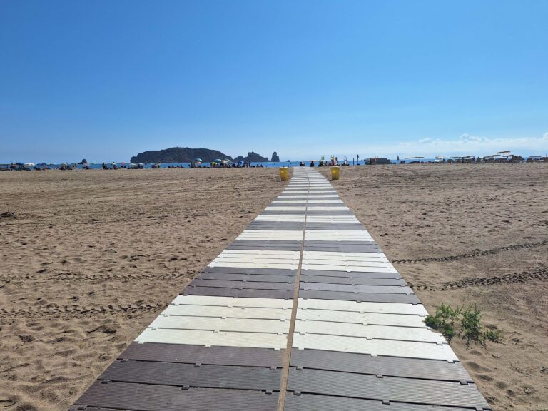 socorrista que acompanya a una nena amb una cadira que no és del tot amfíbia però que l'ajuda a estar a peu de sorra de la platja amb l'aigua just davant seu